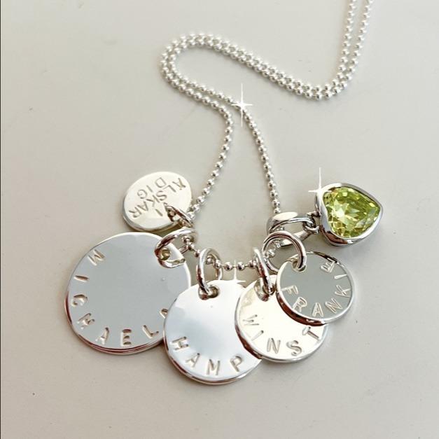 Coin namnhalsband med gravyr i äkta silver med runda namnbrickor med namn på, stansat för hand (inte maskingravyr) samt en röd månadssten för januari månad. Handgjord i Stockholm av silversmed Amanda Egilson