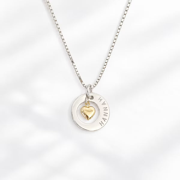 silverhalsband med namn med ett guldhjärta som hänger i mitten av ett utskuret hål. silverkedja.
