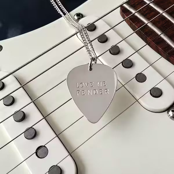 Silverhalsband med plektrum, där ord är instansade för hand. Äkta silver. Smycket ligger på en gitarr.